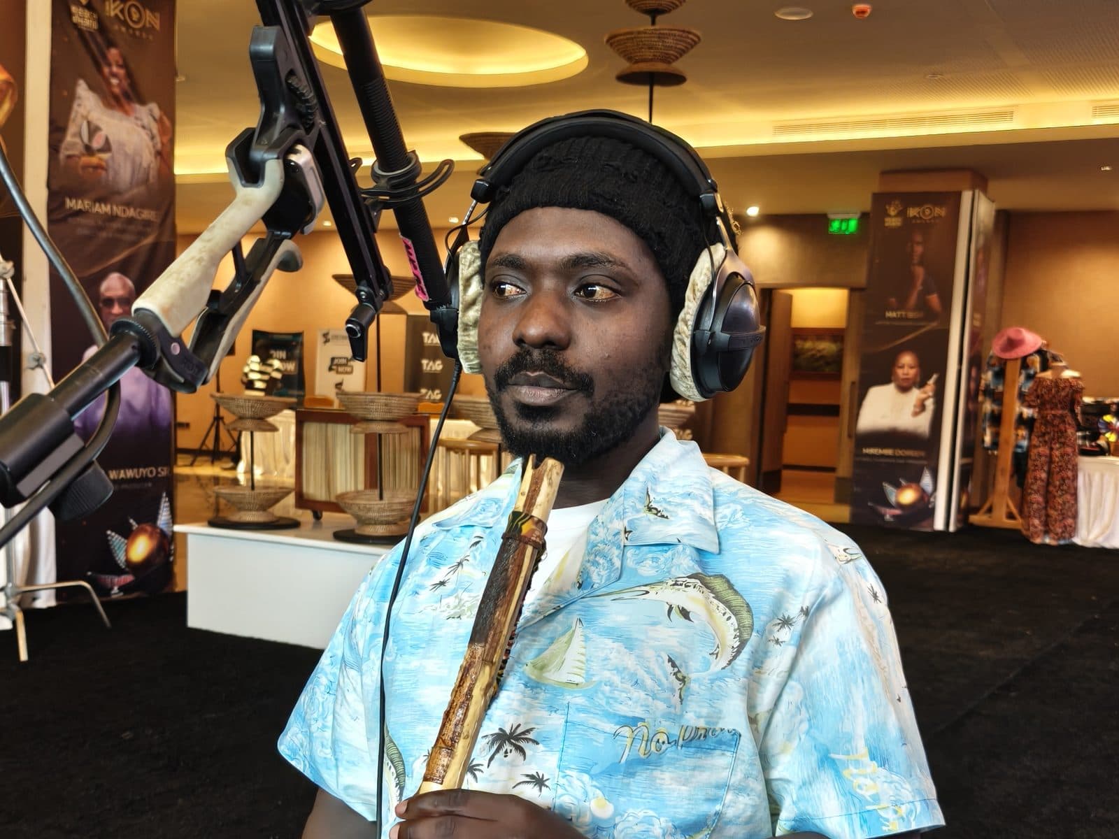A musician playing the endeere, a traditional Ugandan flute, into a studio microphone while wearing headphones